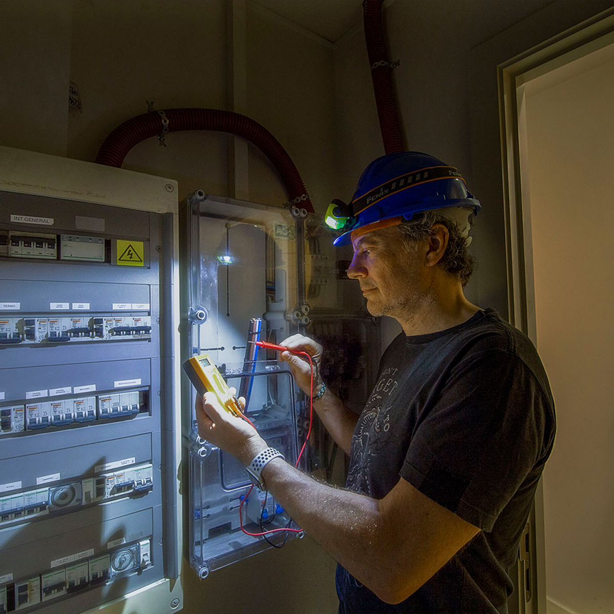 Elektrikár pracujúci na elektroinštalácii s LED čelovkou Fenix.